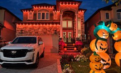 Stone house at night with orange lights on every roofline and Halloween pumpkins on the lawn, one of our installs