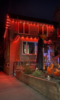 House at night with orange permanent lights along the roofline and down a corner for Halloween, one of our installs