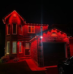 Two-storey brick house at night with red permanent lights on every roofline, one of our installs