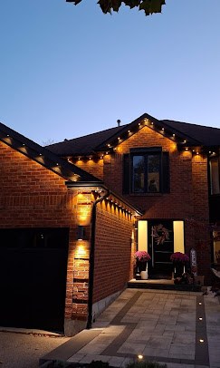Brick house at dusk with warm white permanent lights along the roofline, one of our installs